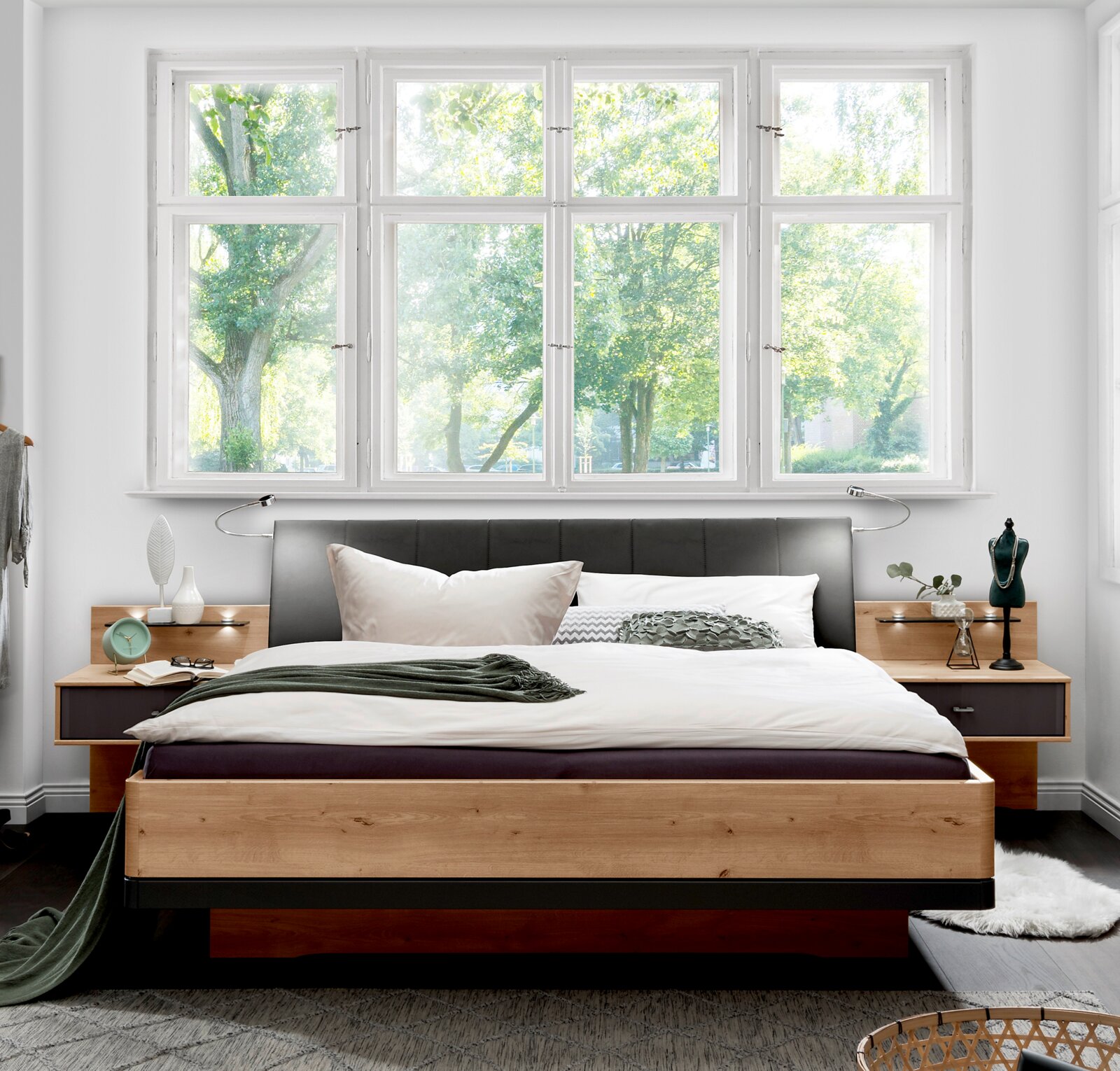 Modern houten futonbed met gestoffeerd hoofdeinde, geflankeerd door nachtkastjes, in een lichte kamer met grote ramen, vooraanzicht