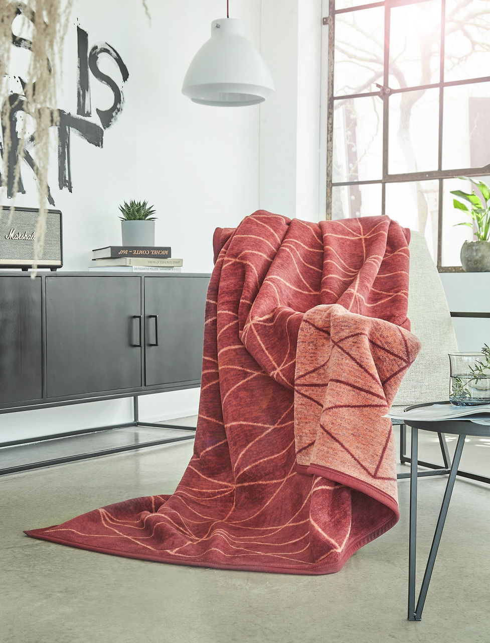 Rote Jacquard-Decke 150x200 cm mit Blattmuster, drapiert über einem Sessel in einem modernen Wohnzimmer mit Blick auf Fenster und Dekoration.