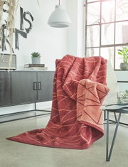 Rote Jacquard-Decke 150x200 cm mit Blattmuster, drapiert über einem Sessel in einem modernen Wohnzimmer mit Blick auf Fenster und Dekoration.