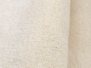 Nahaufnahme eines weichen, cremefarbenen Teppichs mit flauschiger Textur, seitliche Perspektive.