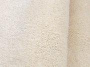 Nahaufnahme eines weichen, cremefarbenen Teppichs mit flauschiger Textur, seitliche Perspektive.