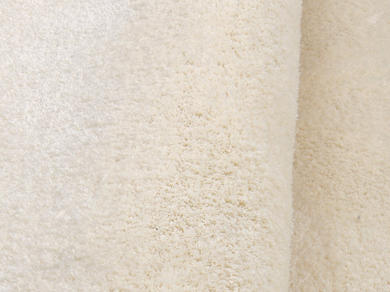 Nahaufnahme eines weichen, cremefarbenen Teppichs mit flauschiger Textur, seitliche Perspektive.