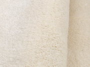 Nahaufnahme eines weichen, cremefarbenen Teppichs mit flauschiger Textur, seitliche Perspektive.