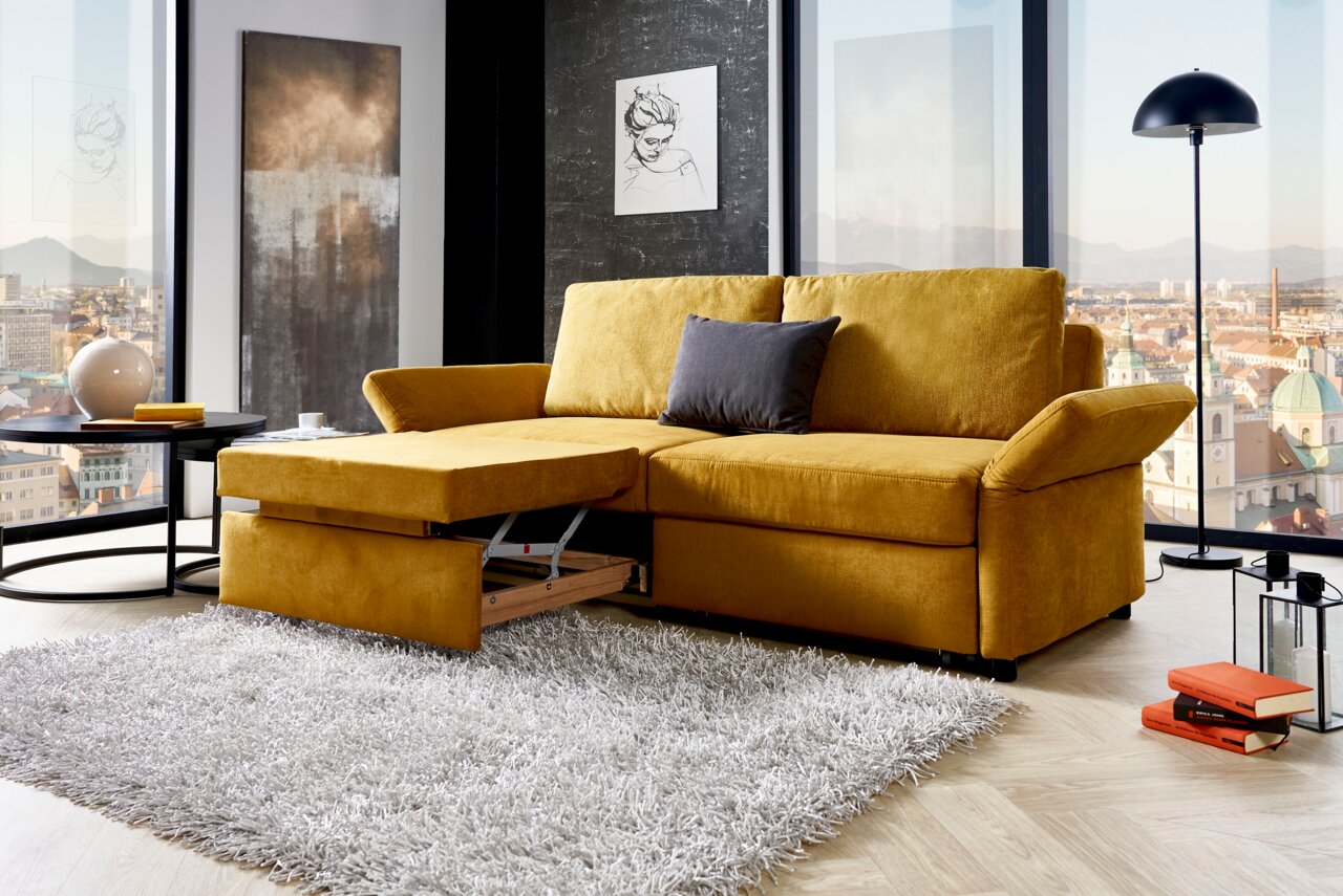 Gelbes Funktionssofa in modernem Wohnzimmer mit Stadtblick, von vorne betrachtet.