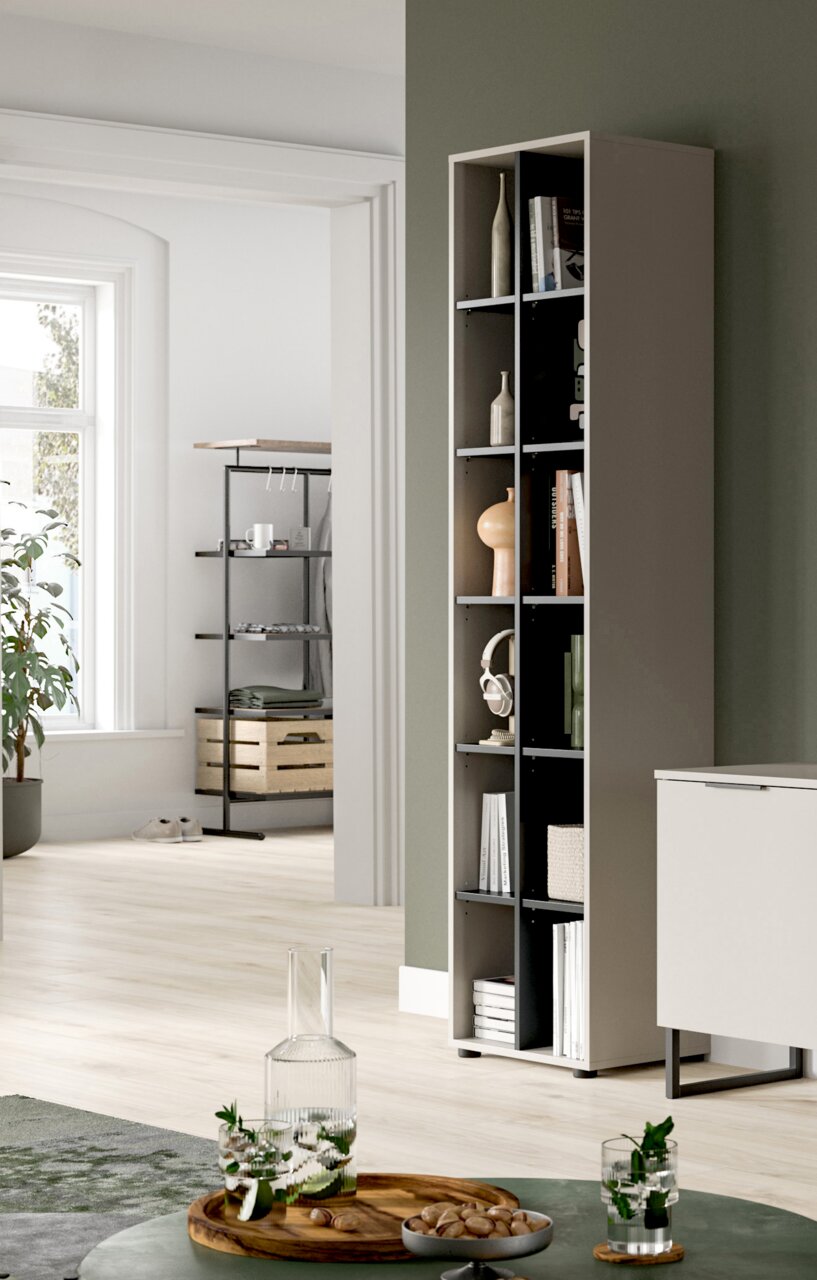 Schmales, hohes Regal in Taupe mit offenen Fächern und Deko, in modernem Wohnraum an grüner Wand, perspektivisch in leichter Seitenansicht von vorn rechts