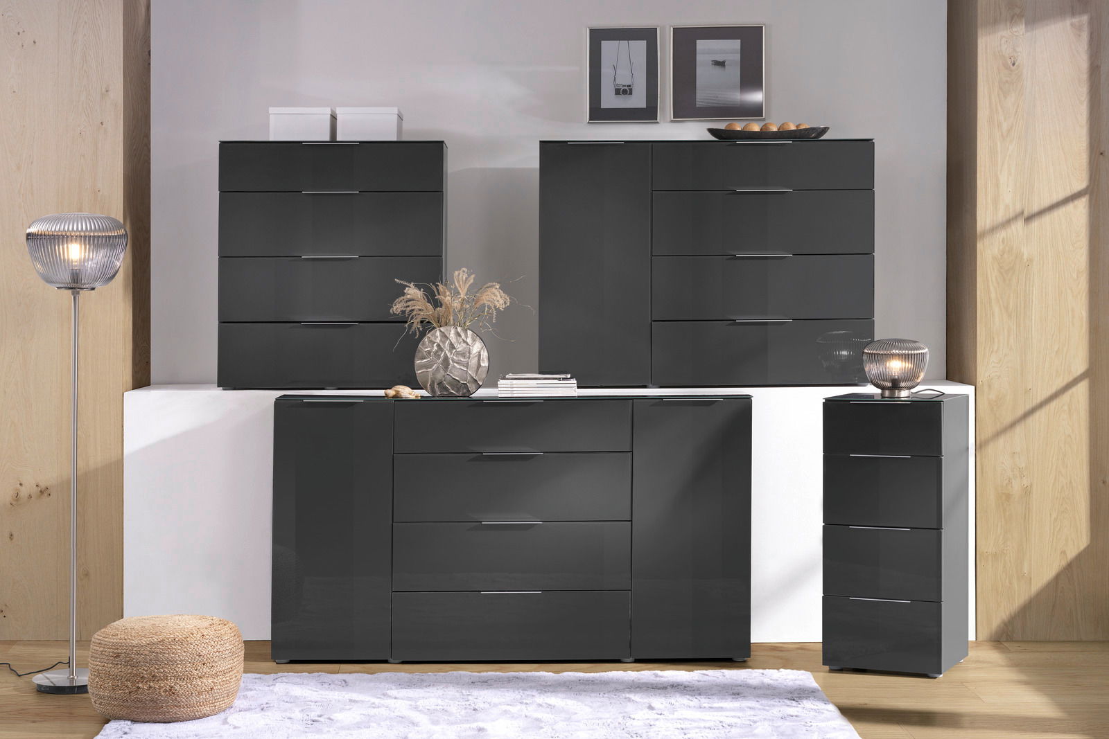 Voleo Ladekast MALIN Moderne schwarze Kommoden in einem stilvollen Raum, frontal betrachtet, mit dekorativen Elementen wie einer Lampe, einem Teppich und Wandbildern.