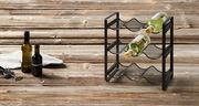 Flaschenregal aus schwarzem Metall mit drei Ebenen, seitliche Perspektive, auf rustikalem Holztisch mit zwei Weinflaschen.
