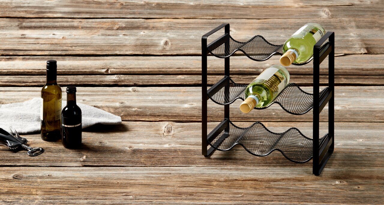 Flaschenregal aus schwarzem Metall mit drei Ebenen, seitliche Perspektive, auf rustikalem Holztisch mit zwei Weinflaschen.