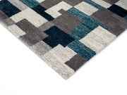 Frisé-Teppich mit geometrischem Muster in Blau-, Grau- und Weißtönen, perspektivisch von der Ecke aufgenommen.