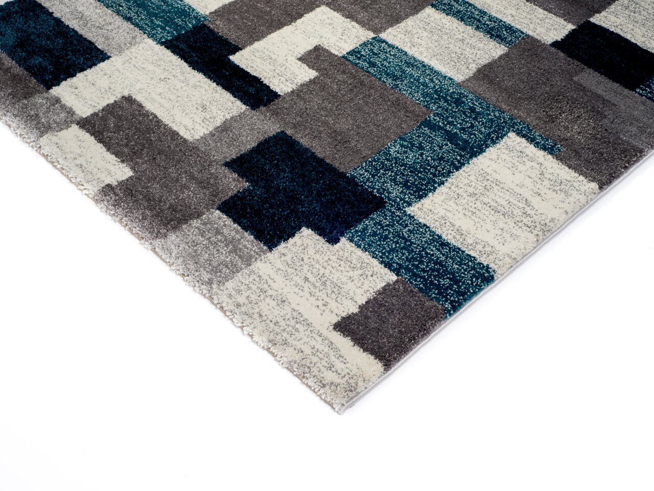 Frisé-Teppich mit geometrischem Muster in Blau-, Grau- und Weißtönen, perspektivisch von der Ecke aufgenommen.
