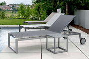 Moderne Rollenliege aus Metall mit verstellbarer Rückenlehne, seitliche Perspektive am Pool mit grüner Landschaft im Hintergrund.