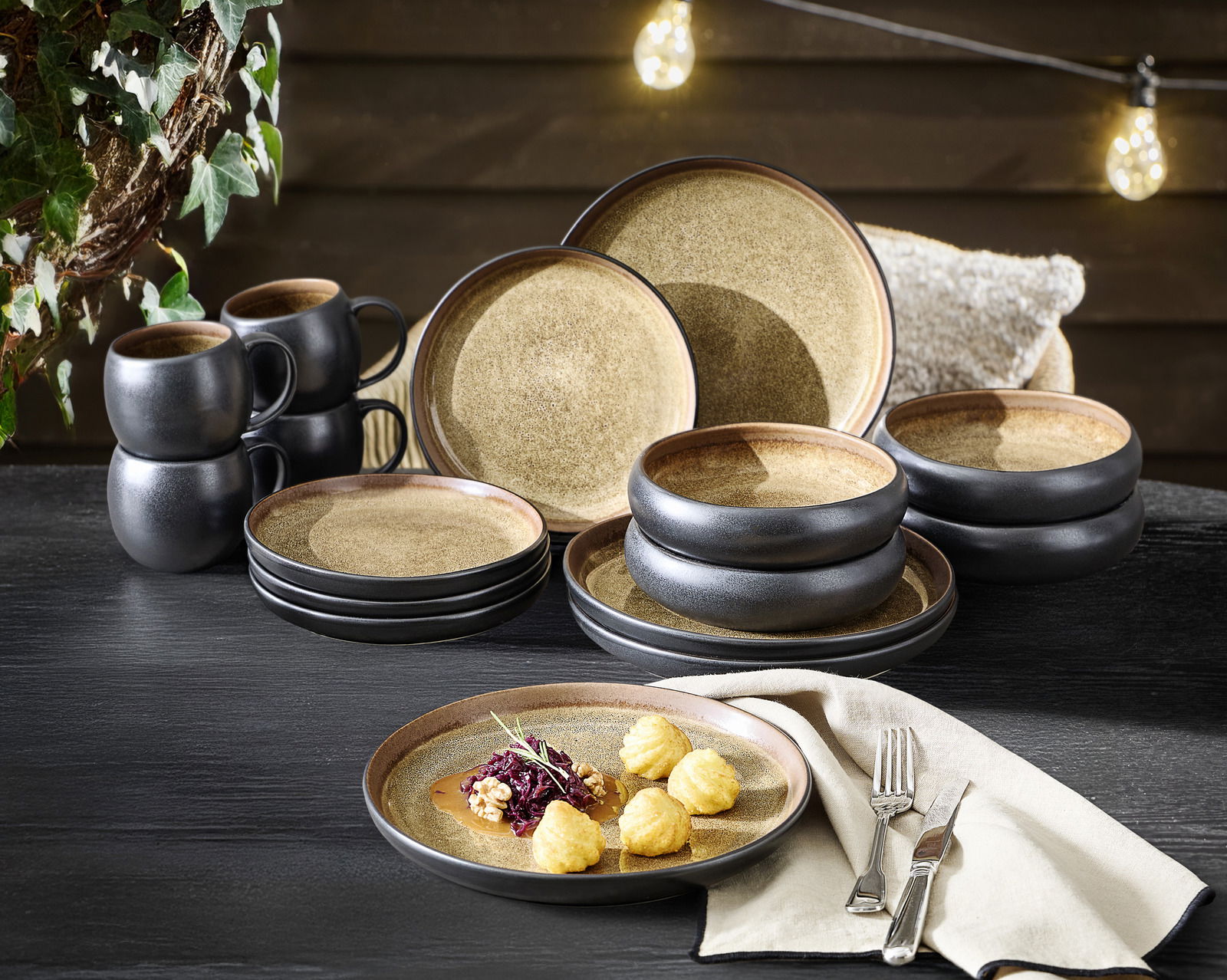 Kombiservice 16-tlg. in rustikalem Design mit schwarzem und braunem Finish, bestehend aus Tellern, Schalen und Tassen, auf einem Tisch arrangiert. Perspektive von vorne.