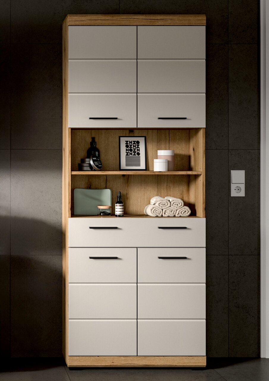 Hoher Badezimmer-Hochschrank in Holzoptik mit weißen Fronten und schwarzen Griffen, mittigem offenem Regal mit Deko und Handtüchern, frontale Ansicht