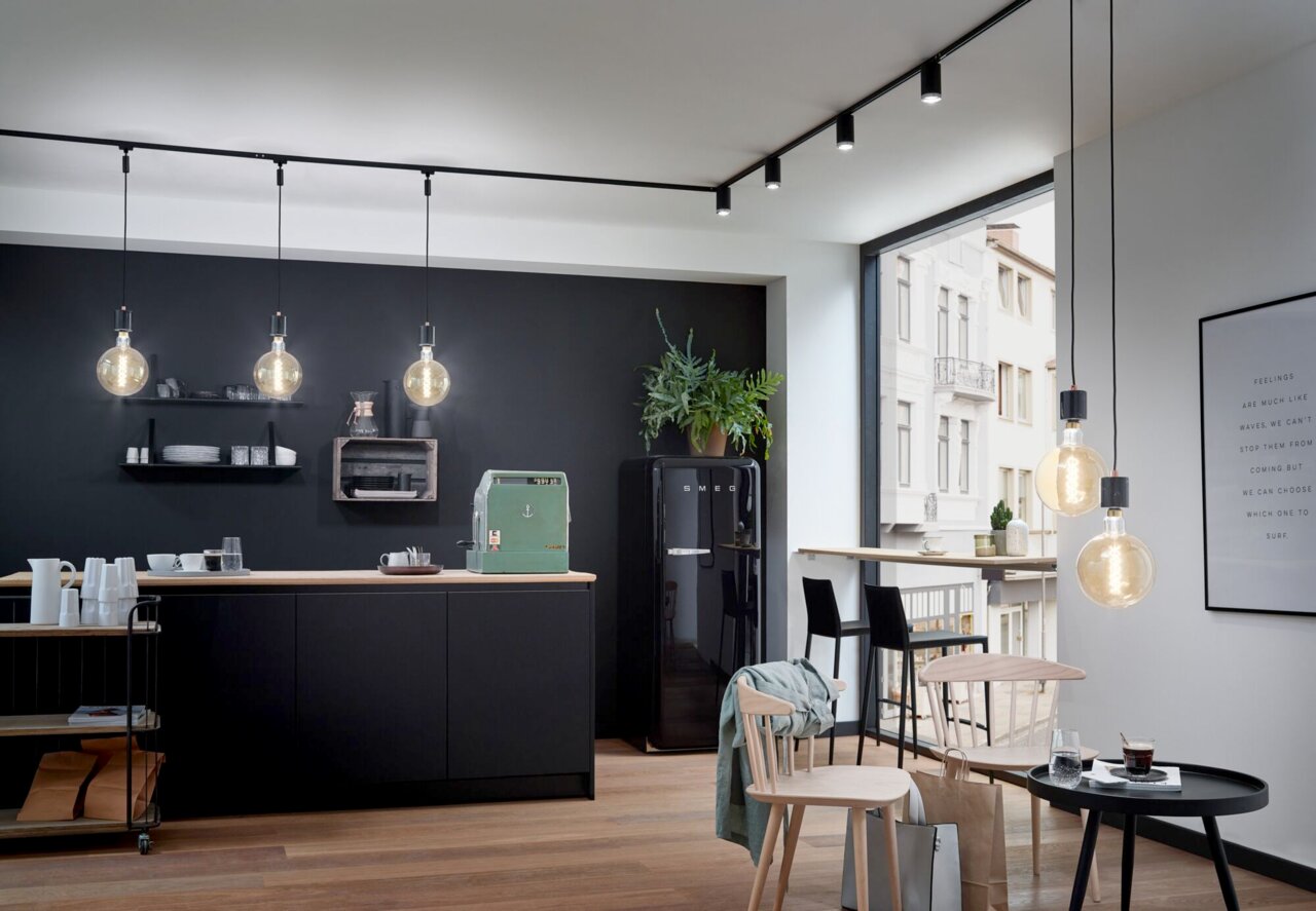 Moderne Küche mit schwarzen Hängelampen an einer Schiene, seitliche Perspektive.