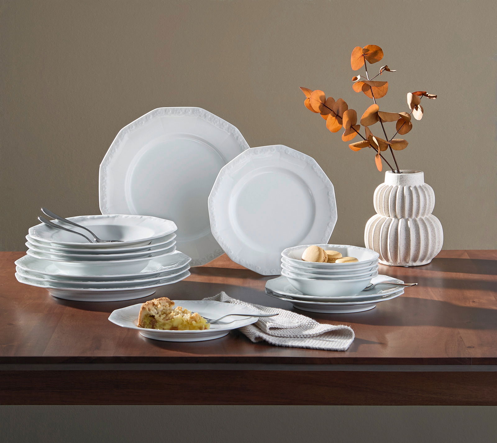 Rosenthal Kombiservice 16-tlg. MARIA WEISS Kombiservice Maria Weiß 16-tlg auf einem Tisch, seitliche Perspektive, bestehend aus weißen Tellern und Schalen mit dezentem Muster, dekoriert mit einem Strauß getrockneter Blätter in einer Vase.
