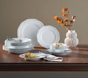 Kombiservice Maria Weiß 16-tlg auf einem Tisch, seitliche Perspektive, bestehend aus weißen Tellern und Schalen mit dezentem Muster, dekoriert mit einem Strauß getrockneter Blätter in einer Vase.