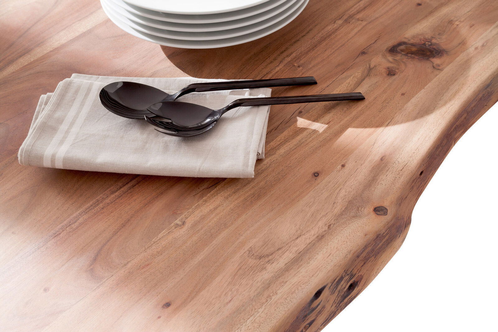 Nahaufnahme eines Esstisches aus Holz mit natürlicher Maserung, darauf liegen gestapelte Teller, ein Stoffserviette und Besteck. Perspektive von oben.