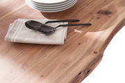 Nahaufnahme eines Esstisches aus Holz mit natürlicher Maserung, darauf liegen gestapelte Teller, ein Stoffserviette und Besteck. Perspektive von oben.