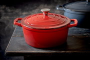 Roter runder Bräter aus Gusseisen mit Deckel, seitliche Perspektive auf einem Holztisch