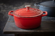 Roter runder Bräter aus Gusseisen mit Deckel, seitliche Perspektive auf einem Holztisch