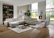 Modernes hellgraues L-förmiges Ecksofa mit Chaiselongue in einem hellen Wohnzimmer mit Couchtisch, Teppich und Sessel; Perspektive: frontale Weitwinkelansicht leicht von links.