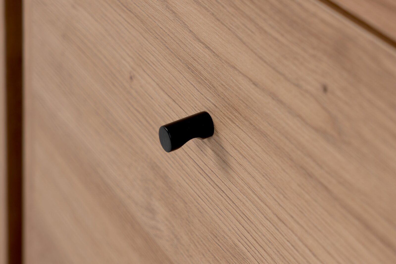 Close-up van een houten kast met een zwarte handgreep, gezien vanaf de zijkant