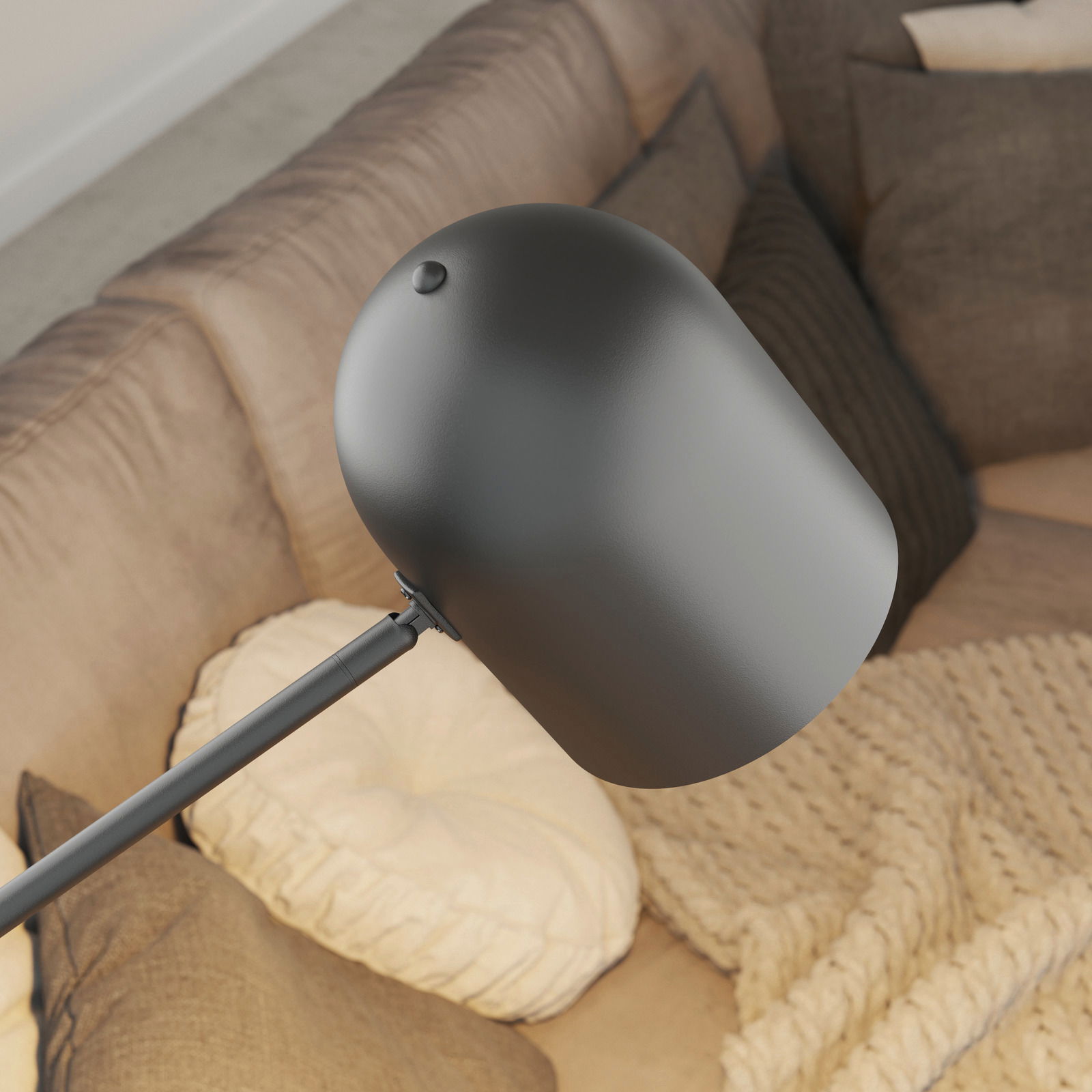 Moderne schwarze Stehleuchte mit abgerundetem Lampenschirm, von oben betrachtet, über einem gemütlichen Sofa mit Kissen.
