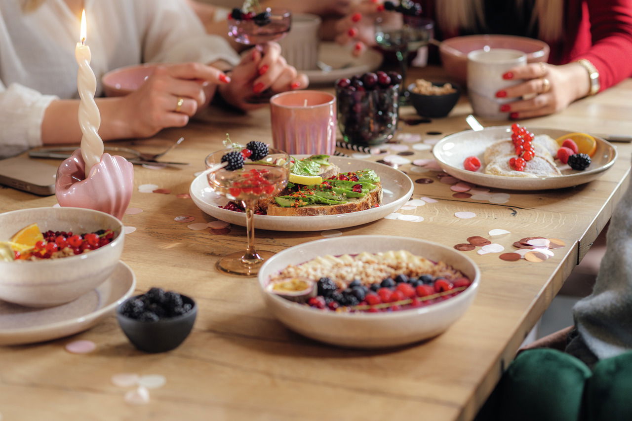 Ein stilvoll gedeckter Tisch mit einer Sekt- und Dessertschale im Vordergrund, gefüllt mit Beeren. Die Perspektive zeigt eine gemütliche, gesellige Atmosphäre.