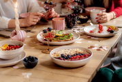 Ein stilvoll gedeckter Tisch mit einer Sekt- und Dessertschale im Vordergrund, gefüllt mit Beeren. Die Perspektive zeigt eine gemütliche, gesellige Atmosphäre.