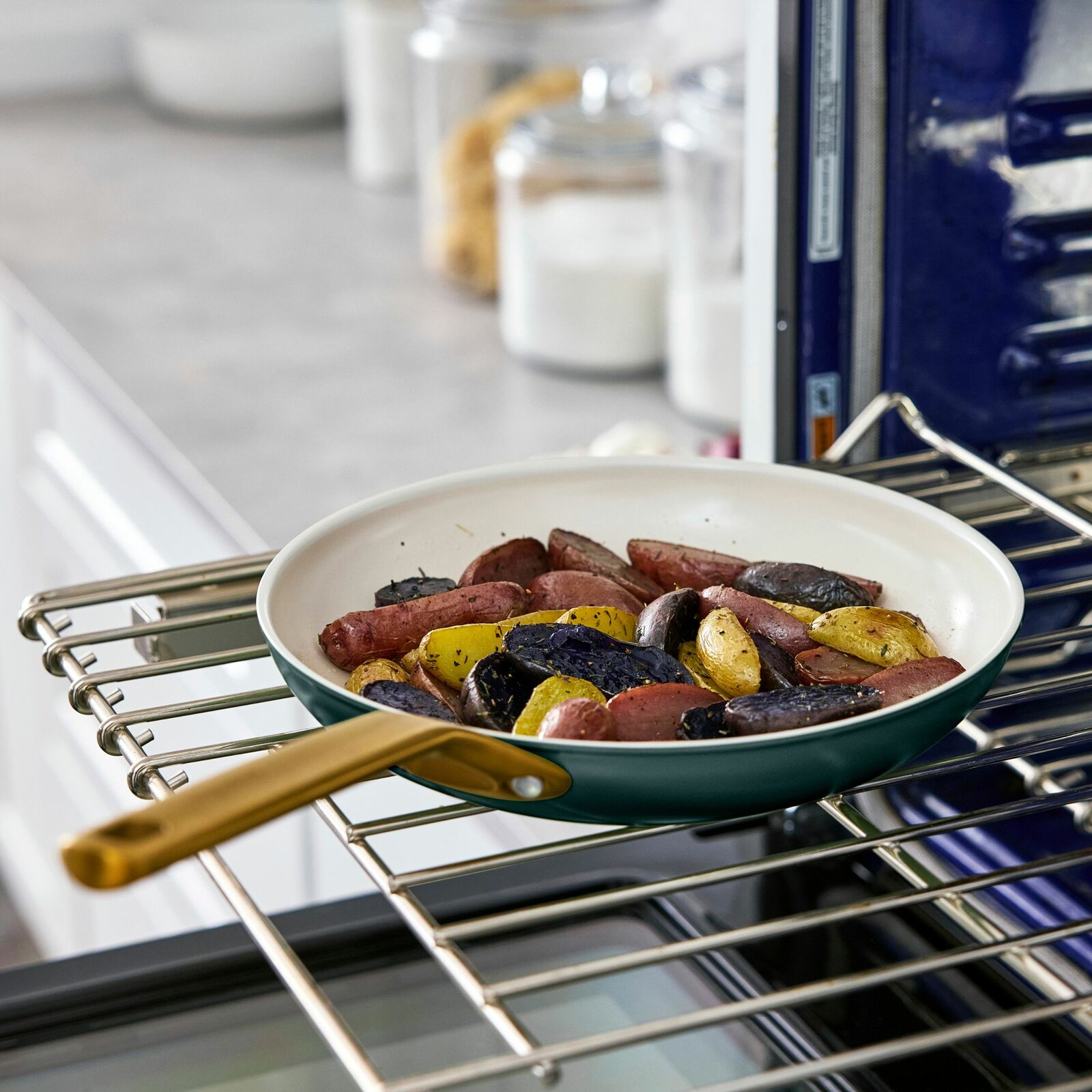Bratpfanne mit goldfarbenem Griff, gefüllt mit gerösteten Kartoffeln, auf einem Ofengitter von schräg oben fotografiert.