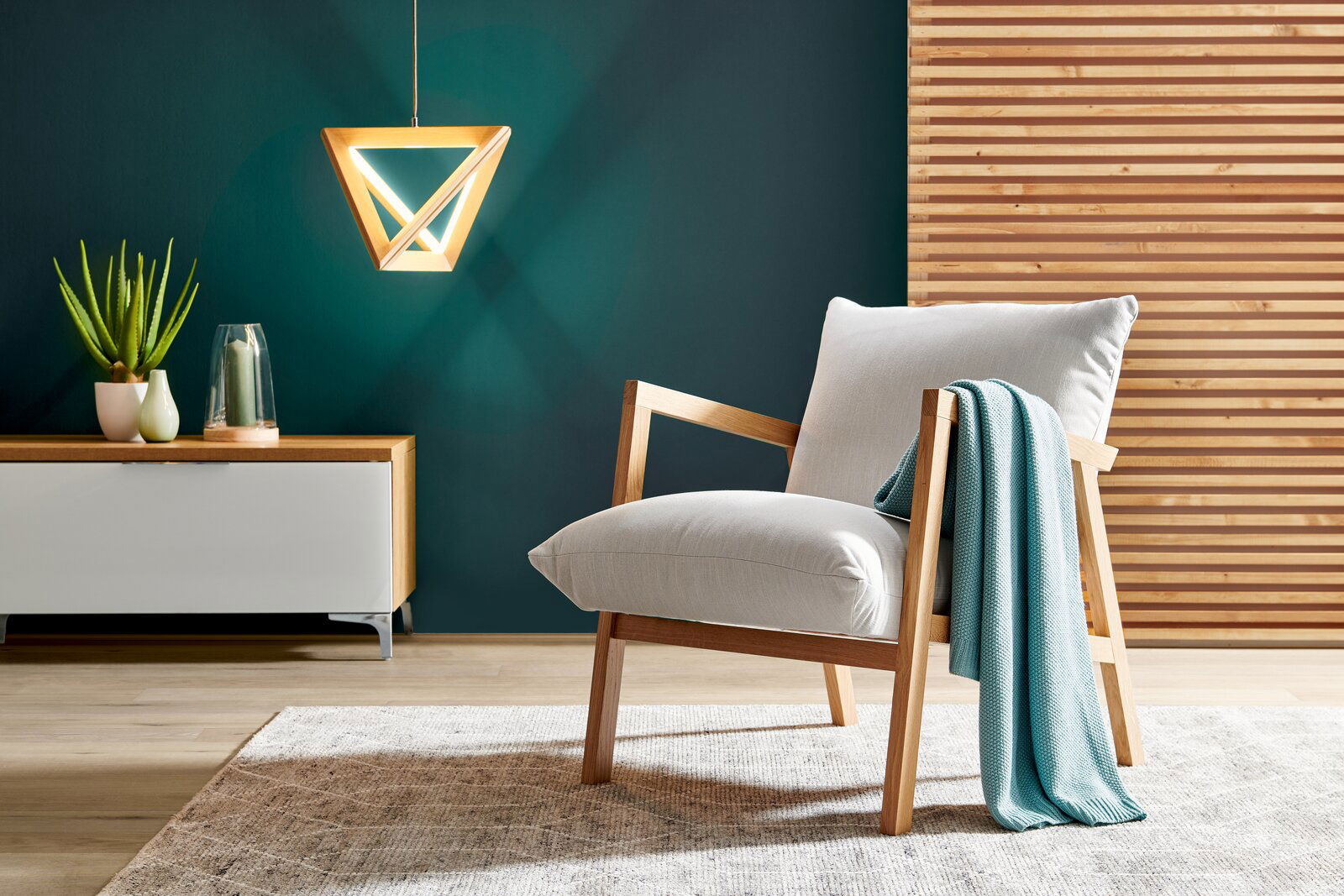 Moderner Sessel mit Holzrahmen und hellgrauem Polster, dekoriert mit einer türkisfarbenen Decke, in einem stilvollen Wohnzimmer mit hölzernem Wandpaneel und hängender Lampe, seitliche Perspektive.