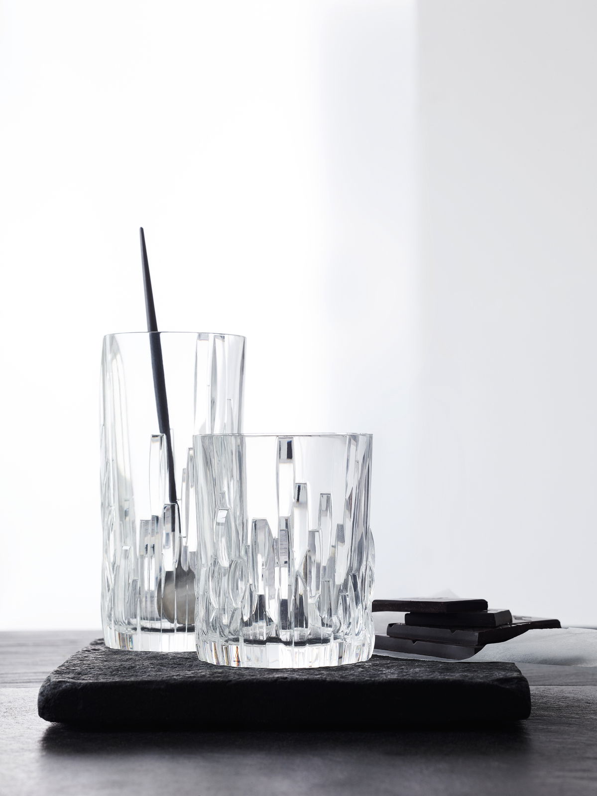 Zwei Longdrinkbecher Shu Fa aus Kristallglas mit modernem, geometrischem Design, auf einer dunklen Unterlage stehend, seitliche Perspektive.