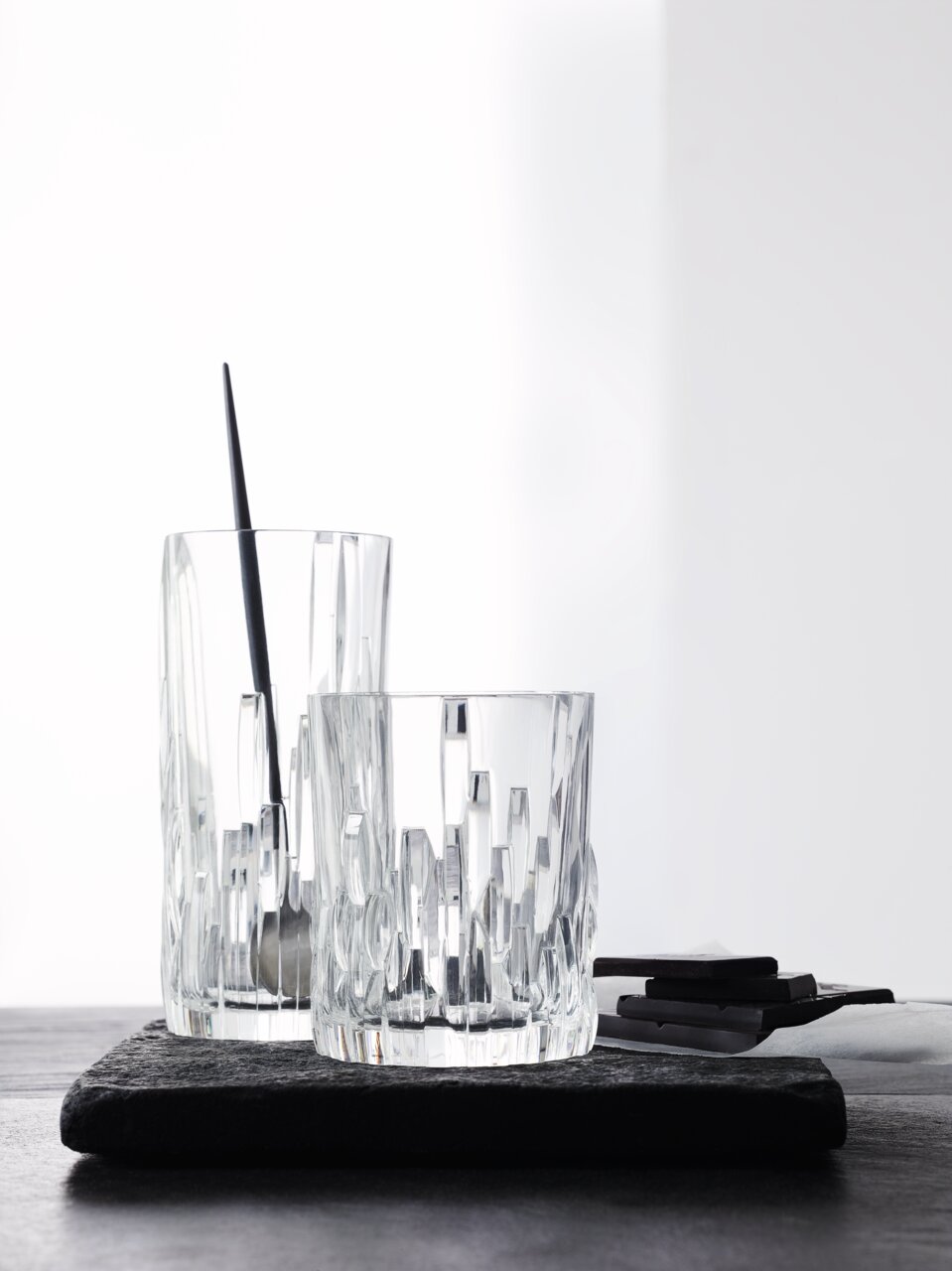 Zwei Longdrinkbecher Shu Fa aus Kristallglas mit modernem, geometrischem Design, auf einer dunklen Unterlage stehend, seitliche Perspektive.