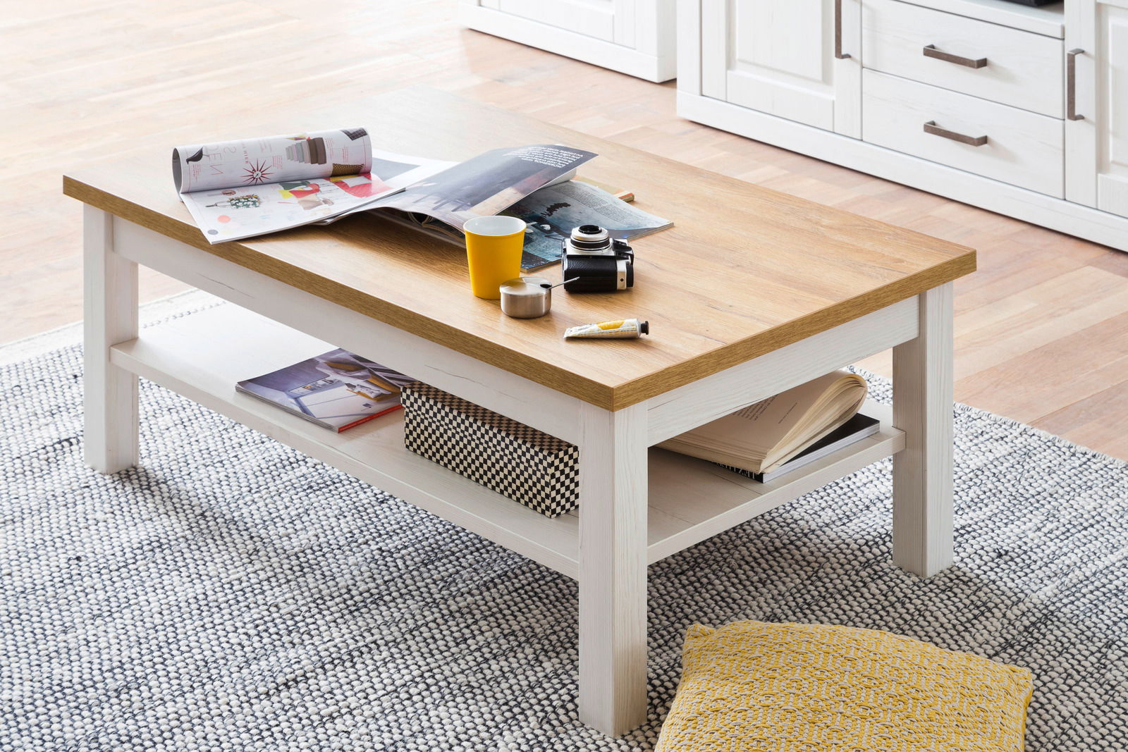 Moderner Couchtisch mit Holzplatte und weißem Gestell, von schräg oben fotografiert, mit Dekorationen wie Zeitschriften, Kamera und Tasse.
