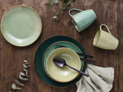 Kombiservice 16-tlg in verschiedenen Grüntönen, bestehend aus Tellern, Schalen und Tassen, auf einer Holzoberfläche von oben fotografiert.