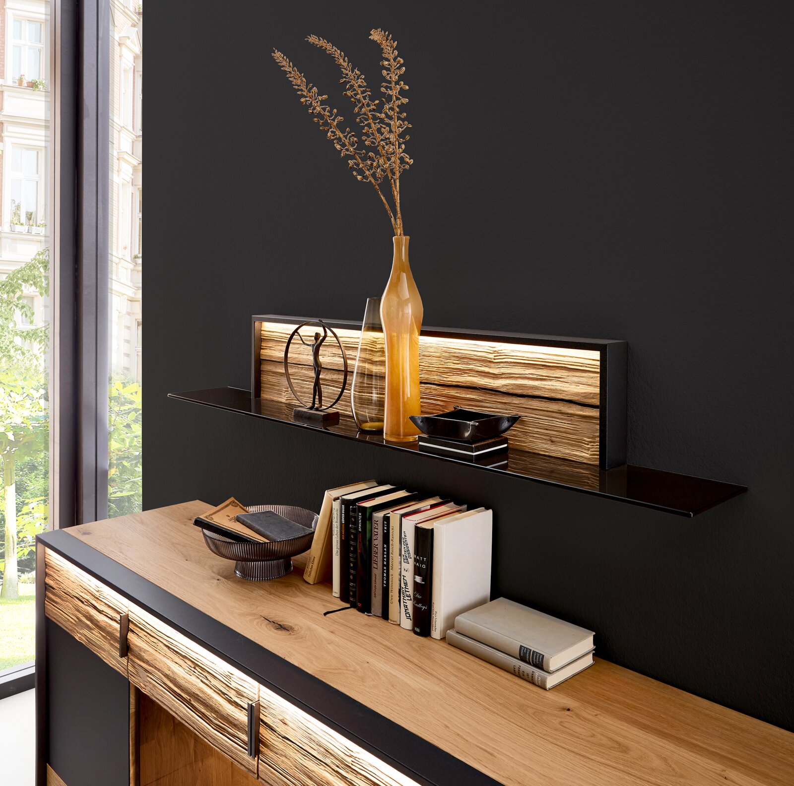 Modern houten dressoir met zwart frame en verlichte wandplank, versierd met een vaas, boeken en schalen; perspectief: licht schuin van voren.