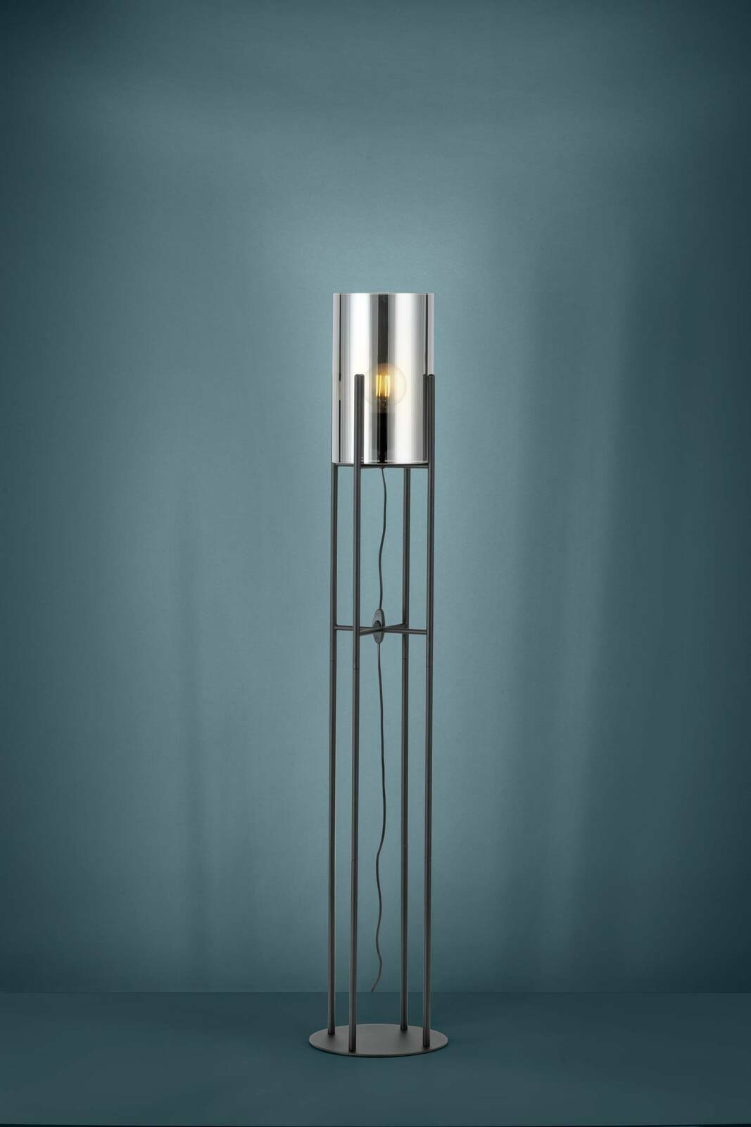 Moderne Stehleuchte GLASTONBURY mit zylindrischem Lampenschirm aus Metall, frontal abgebildet vor einem blauen Hintergrund.