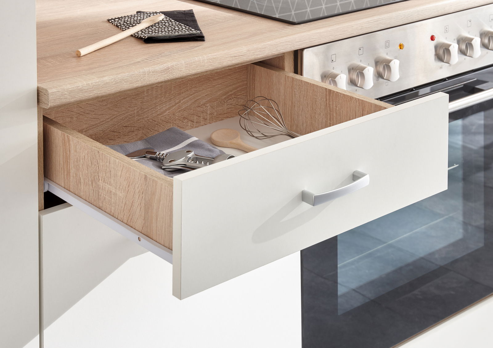 Nahaufnahme einer geöffneten Küchenschublade mit Küchenutensilien, darunter ein Schneebesen und ein Korkenzieher, in einem modernen Küchenblock.