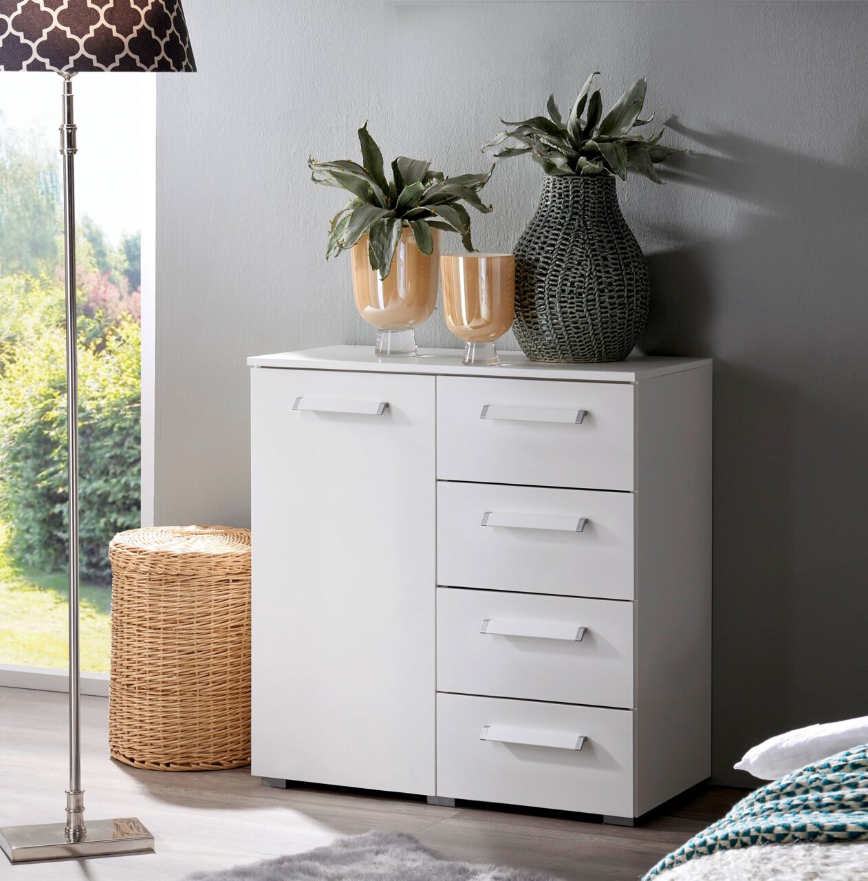 Weiße Kommode mit vier Schubladen und einer Tür, dekoriert mit Pflanzenvasen, aus der Frontalperspektive fotografiert.
