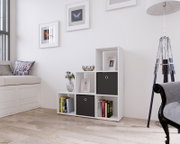 Modernes weißes Würfelregal mit versetzten Fächern, zwei schwarzen Stoffboxen und Büchern im hellen Wohnzimmer; Perspektive: frontale Ansicht auf Augenhöhe.