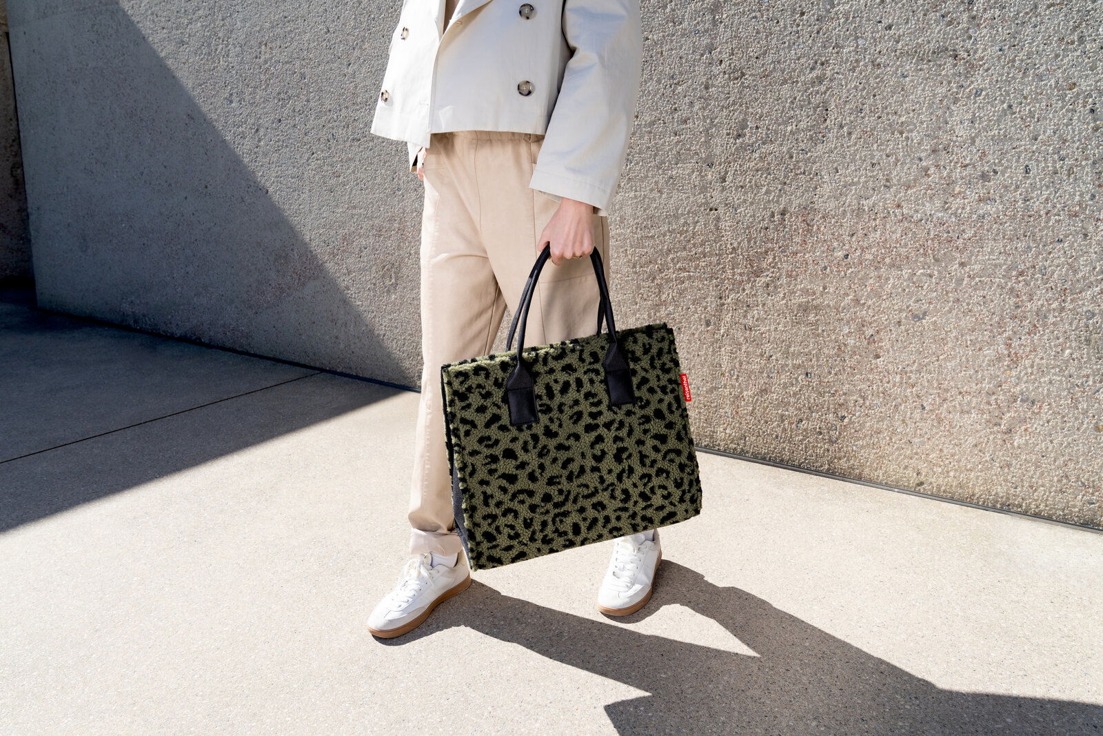 Person hält eine grüne Tasche mit Leopardenmuster in der Hand, seitliche Perspektive