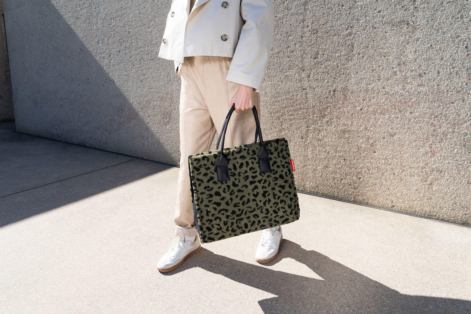 Person hält eine grüne Tasche mit Leopardenmuster in der Hand, seitliche Perspektive