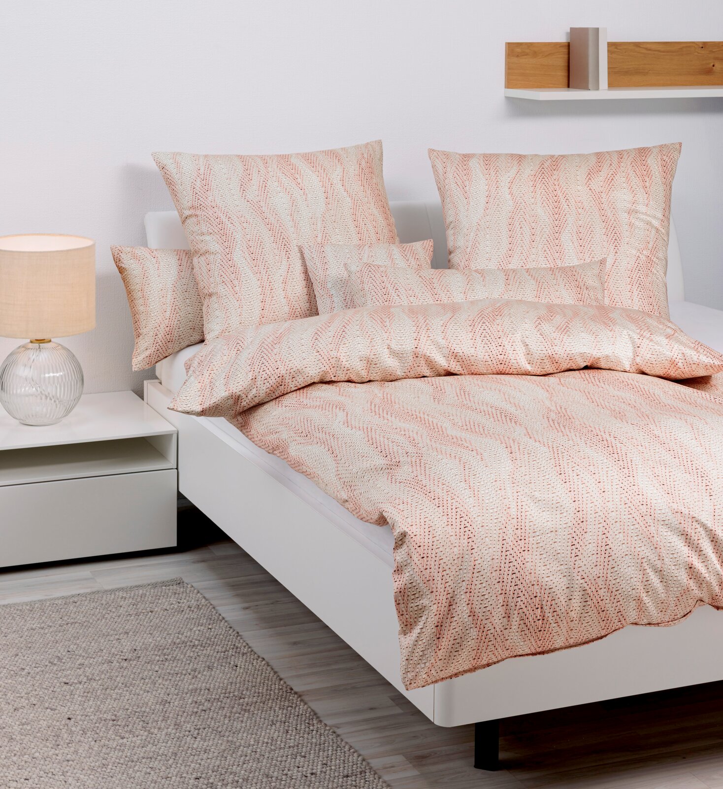 Bettwäsche-Set in sanften Beige- und Rosatönen mit wellenförmigem Muster, auf einem modernen weißen Bett präsentiert, seitliche Perspektive