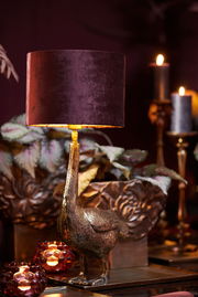 Eleganter Lampenschirm in dunklem Samt, getragen von einer goldenen Vogelstatue, seitliche Perspektive.