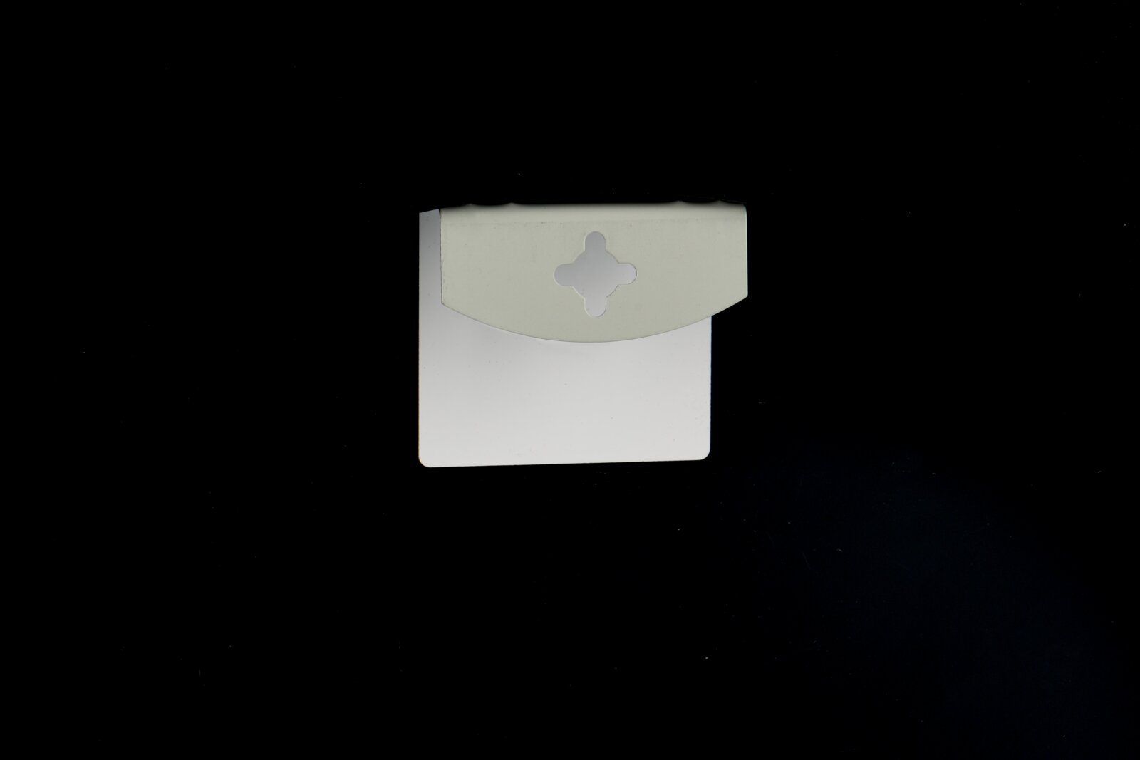 Weiße, rechteckige Verpackungskarte mit grauem Aufhänger/Lasche und Kleeblatt-förmiger Stanzung, frontal von oben auf schwarzem Hintergrund fotografiert