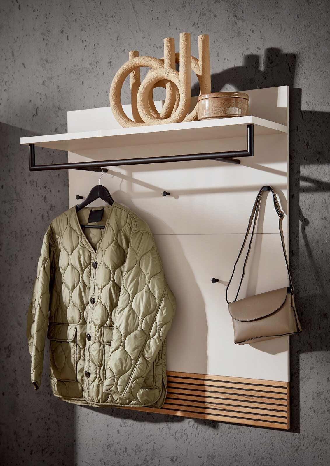 Garderobenpaneel mit Haken und Ablage, darauf eine Jacke und eine Tasche, seitliche Perspektive