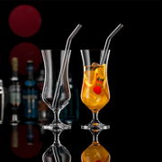 Zwei elegante Cocktailgläser mit Trinkhalm, eines leer und eines gefüllt mit einem Getränk und einer Kirsche, vor einem dunklen Hintergrund mit Flaschen im Hintergrund, seitliche Perspektive.