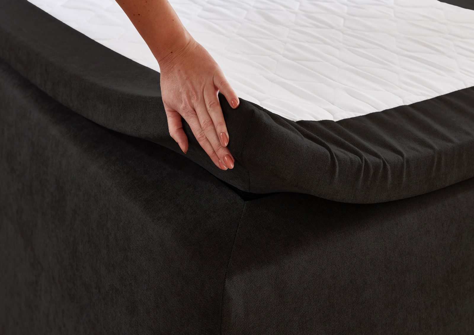 Nahaufnahme einer Hand, die die Matratze eines Boxbetts anhebt, um die Qualität und den Stoff zu zeigen.