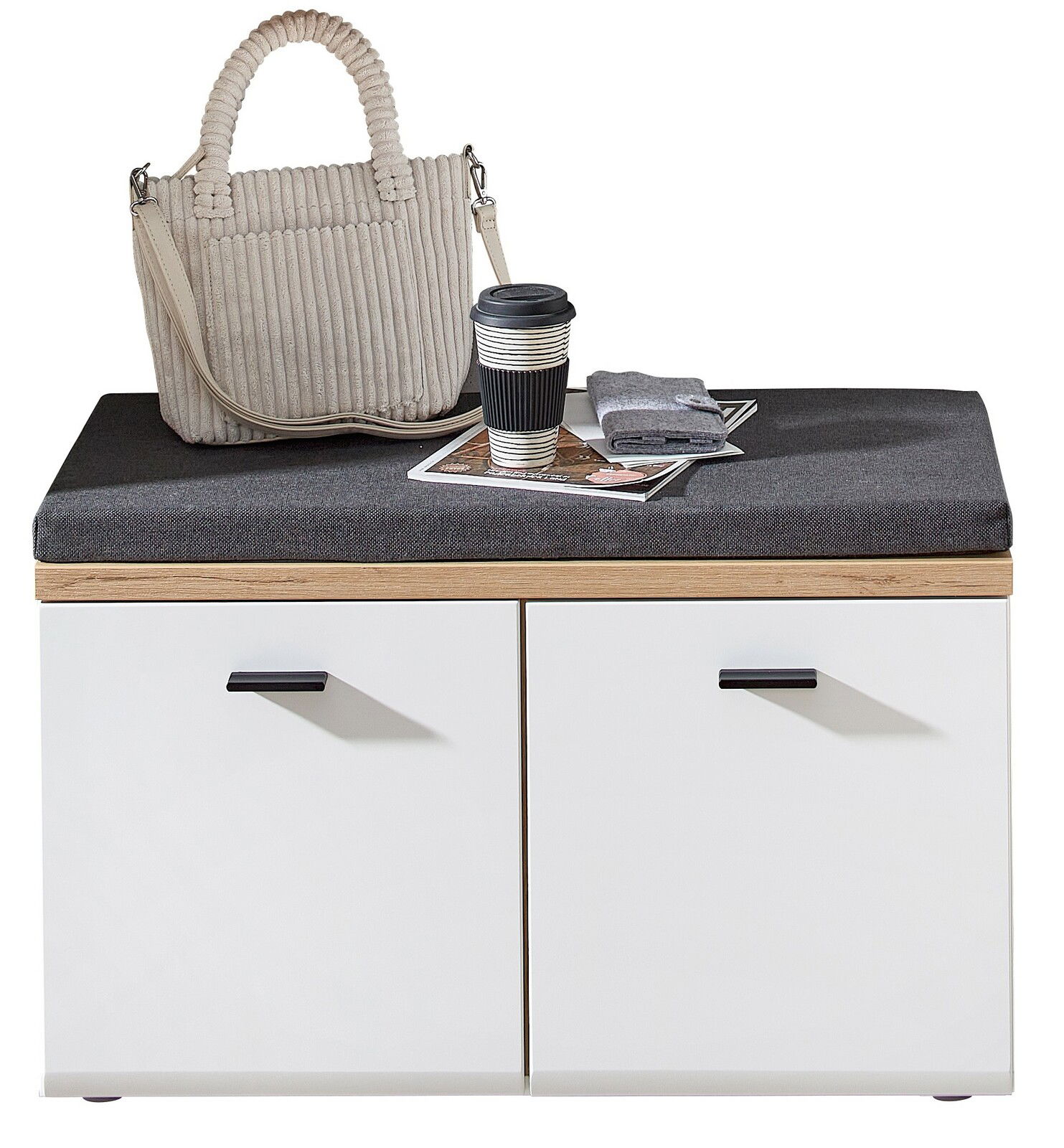 Garderobenbank mit weißem Korpus, Holzdetails und grauem Sitzpolster, darauf eine beige Handtasche, ein Kaffeebecher und Zeitschriften, Perspektive von vorne.