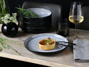 Elegantes Tafelservice mit schwarzem und grauem Design, präsentiert auf einem Holztisch mit einem Quiche, Besteck, einem Weinglas und einer Vase mit Blumen, aus der Vogelperspektive.